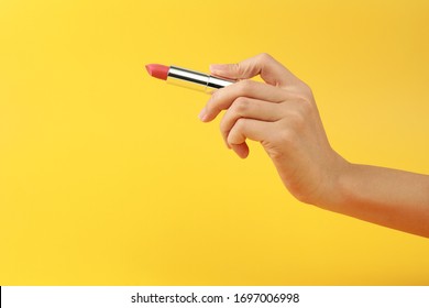 Woman hand holding red lipstick on yellow background