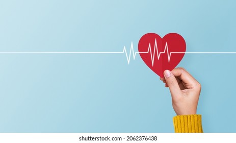 Woman hand holding red paper heart with cardiogram on blue background. Concept of valentines day, love, health care
