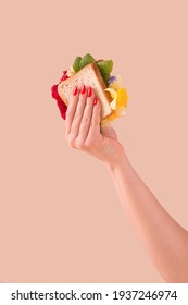 Woman hand holding sandwich with fresh colorful flowers on pastel background. Creative spring or summer concept.