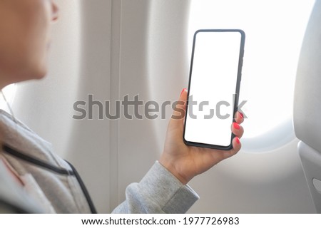 woman hand holding smart cell phone with blank white screen on board of airplane near window seat. Woman Using Mobile Phone While Sitting In Airplane. Woman using smartphone in airplane during flight