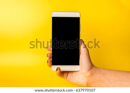 Woman hand holding smartphone on yellow background.