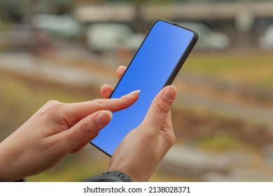 Woman Hand Holding Smartphone Outside And Touching Blue Screen.