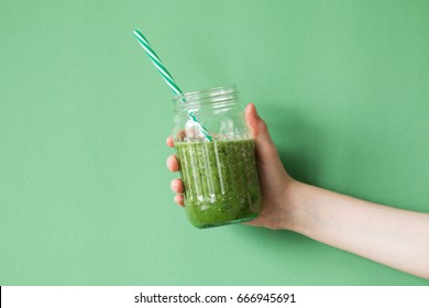 Woman hand holding smoothie shake against colored wall. Drinking green healthy smoothie concept. - Powered by Shutterstock