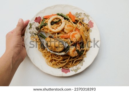 woman hand holding a spicy spaghetti with shrimp, mussel, with pepper, chili, corn,mussel
squid and herbs sauce in plate. spaghetti with spicy mixed seafood and basil.thai fusion food