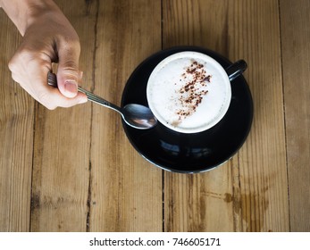 Woman Hand Holding Spoon With Cup Of Cappuccino On Wooden Table Top View