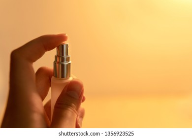 Woman hand holding spray bottle with warm yellow light background.