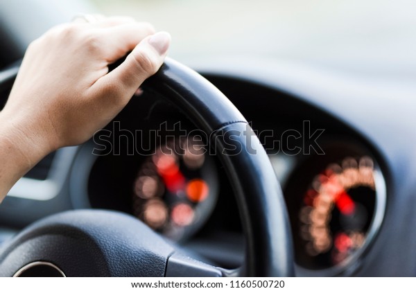 Woman hand
holding steering wheel detail. Modern car dashboard with
speedometer or tachometer in backround.
