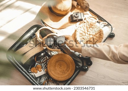 Woman hand holding sunglasses, hat, bag and other things on wooden table. Travel concept.