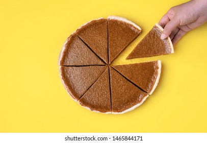 Woman hand holding and taking a piece of pumpkin pie on a yellow background. Above view of traditional autumn dessert. Thanksgiving sweet food. Eating pie.