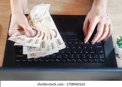 Woman Hand Holding Thai Banknotes And Working On Computer Laptop From Home, Make Money Online,earning,investment Concept                     