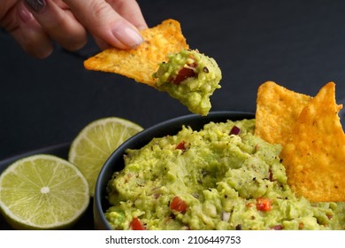 Woman Hand Holding Tortilla Chip Or Nachos With Tasty Guacamole Dip On A Black Background