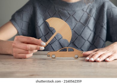 Woman Hand Holding Umbrella And Cover Car Toy On Table. Car Insurance