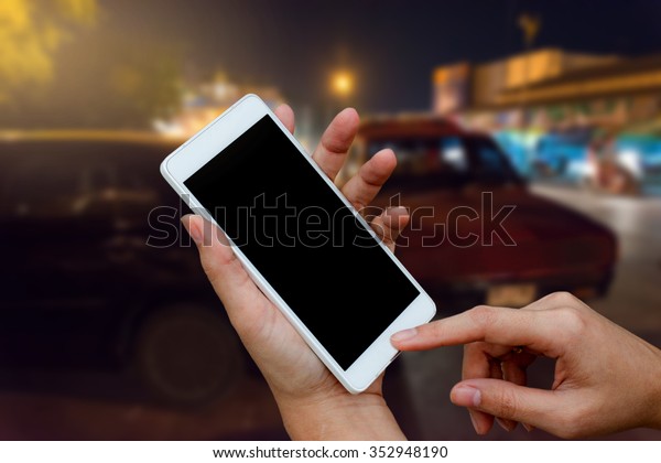 woman hand holding and using mobile\
(smart phone) over blurred image of broken car : calling mechanic\
service from repair shop and insurance\
concept