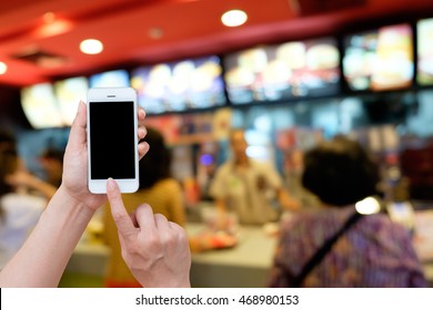 Woman Hand Holding And Using Mobile,cell Phone,smart Phone With Isolated Screen With Blur Image Of A Fast Food Restaurant For Background.