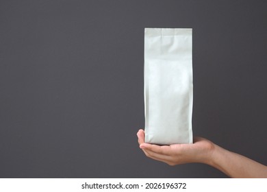Woman Hand Holding White Blank Coffee Bag On Gray Background. Packaging Mockup With Empty Space For You Designs.
