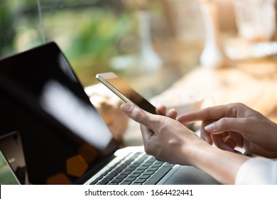 Woman hand holding white mobile phone on a table with a laptop in office. - Powered by Shutterstock