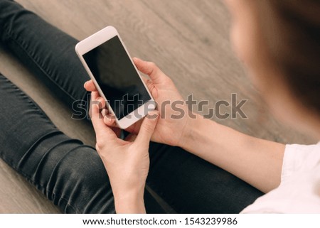 Woman hand holding white mobile phone and sitting on black sofa at home.