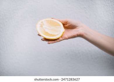 Woman hand holding whole juicy halved lemon on white wall background. - Powered by Shutterstock