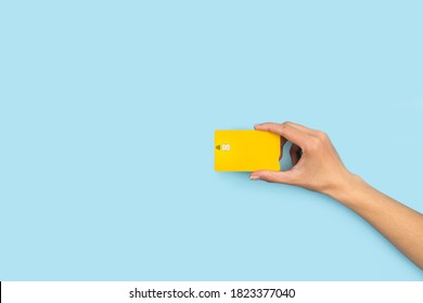 Woman Hand Holding A Yellow Credit Card On A Light Blue Background