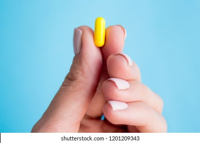 woman hand holding yellow pill capsule on blue background, medication concept with copy space - Powered by Shutterstock