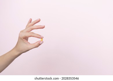 Woman hand holding yellow pill capsule on a pink background, medication concept with copy space. High quality photo