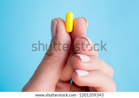 woman hand holding yellow pill capsule on blue background, medication concept with copy space