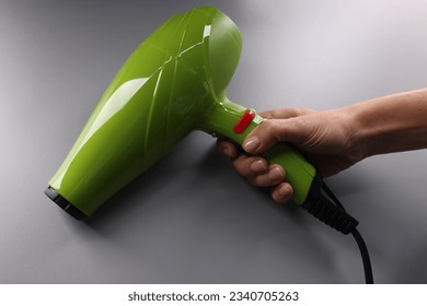 Woman hand holds bright green hair dryer on gray background