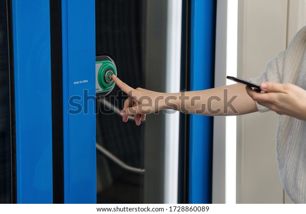 Woman\
hand index finger presses button to open doors in subway car.\
Public transport regulations, responsible\
passenger
