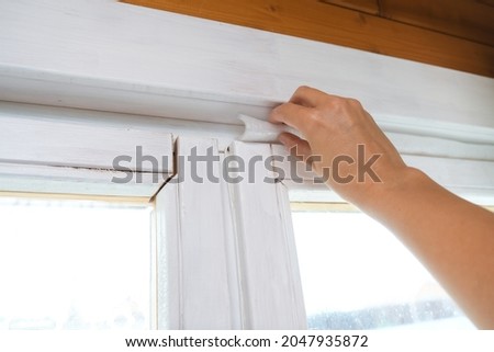 Woman hand insulating old windows to prevent warmth heat leak and drafts, preparing house for winter and cold weather.