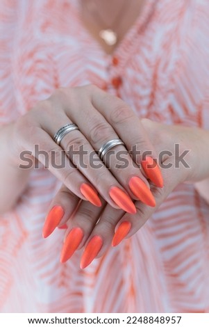 Woman hand with long nails and light orange coral neon manicure holds a bottle of nail polish	