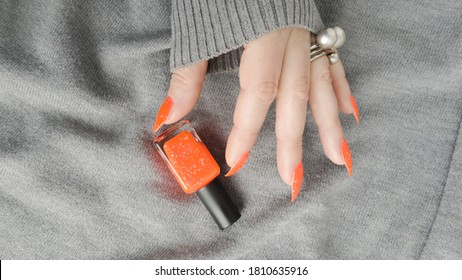 Woman hand and long nails   orange ginger manicure holds bottle nail polish