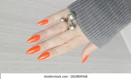 Woman hand and long nails   orange ginger manicure holds bottle nail polish