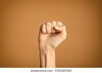 Woman hand making fist sign fighting for her rights. Hand with fingers folded into fist isolated on brown background. Fighting for women rights, against the violence and for equality and independence. - Shutterstock ID 1952587030