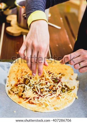 Woman hand is making Homemade traditional Mexican food burrito, fajitas, Quesadillas, Enchiladas or tacos with cheddar cheese on a backing paper, ready for baking in the oven.