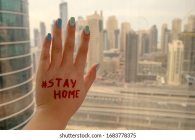 Woman hand on a window with "Stay Home" writing on a blurred Dubai skyscrapers background. Stay Home call during COVID-19 Outbreak. Warning alert, lockdown, curfew