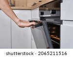 Woman hand open electric oven door with handle. Homemade cooking. Kitchen appliance