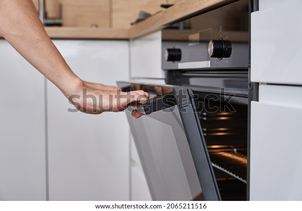 Woman hand open electric oven door with handle.\
Homemade cooking. Kitchen\
appliance
