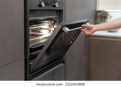 Woman Hand Opening Door Of New Modern  Oven With Light Built-in In Black Kitchen Cabinet