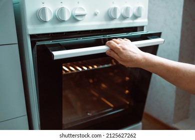 Woman Hand Opening Oven Door In Kitchen At Home. Door Is Open And Light Is On, Home Cooking