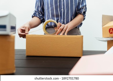 Woman hand packing shipment box with transparency tape on table.