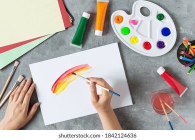 Woman hand painting rainbow in sketchbook with pain brush with art supplies around top view on grey concrete table. Creativity and hobby concept. - Powered by Shutterstock