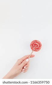 Woman hand with pastel manicure polish holding bright red swirling lollipop isolated on white background copy space minimalism style. Template for feminine social media. Fun and celebration concept