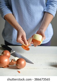 Woman hand peel fresh onion on white table