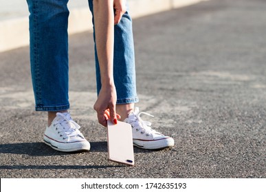 Woman Hand Picking Broken Phone From Asphalt After Drop, Bottom View, Outdoors. Smartphone With Broken Glass On The Back Cover. 