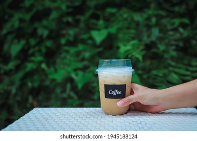 Woman Hand Picking Up Coffee Cup With Blurred Green Background.