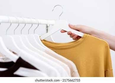 Woman hand picking out clothes to buy hanging on clothing rack in fashion store, close up. Female clothes organized on white clothes hangers. Shopping concept