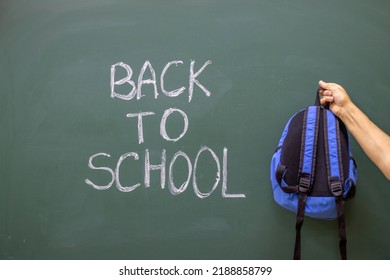 Woman Hand Pointing At Inscription Back To School Holding Blue Backpack For Kids.white Letters On Blackboard Written With White Chalk.mother Granny O Teacher Hand Isolated.ready For First School Day.