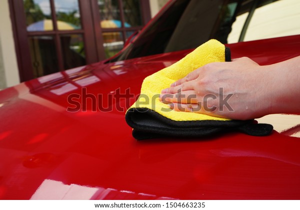 a woman hand polish the red car hood with\
yellow towel after waxing the car for shiny look ,manual car wash\
and hand wash at home by woman\
concept