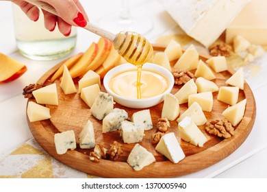 Woman Hand Pouring Honey To Cheese Board Gourmet Side View. Girl Taste French Cheeseboard With Brie, Parmesan And Mozzarella Assorted. Gouda And Walnut Various Dessert Platter