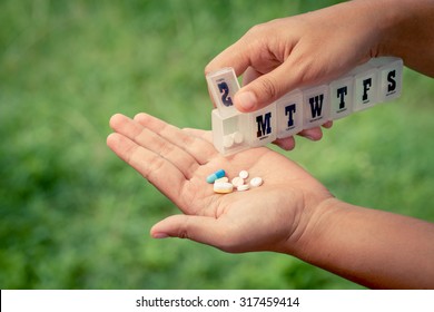 Woman Hand Pouring Pills From A Pill Reminder Box Into Her Hand On Green Nature Background In Vintage Filter